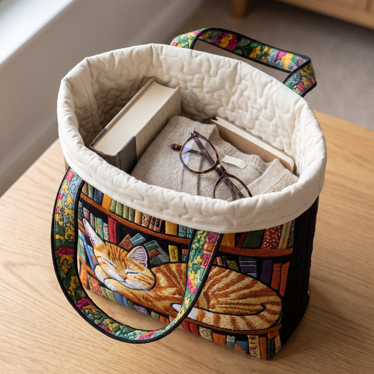 Cat Loves Books Quilted Tote Bag — packed with a hardback book, a folded cardigan and reading glasses